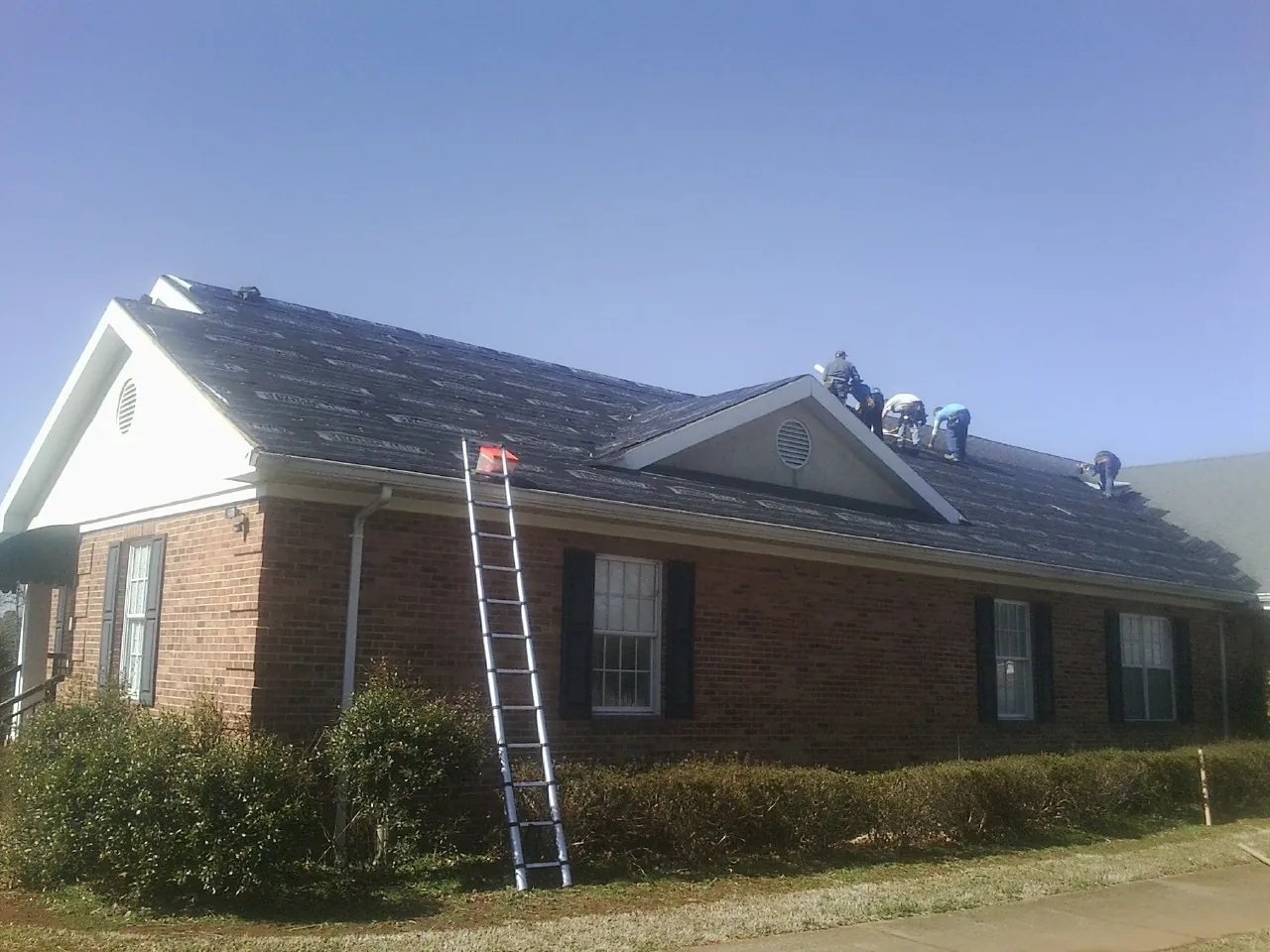Crew tearing shingles off a brick ranch roof with a ladder set — Metal Roof Repair work by our crew in Big Bend