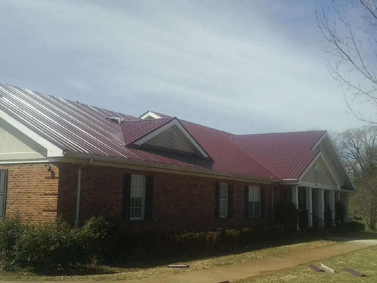 Red metal roof with gabled entries on a long brick building, from a Hail Damage Roof Repair job in Big Bend