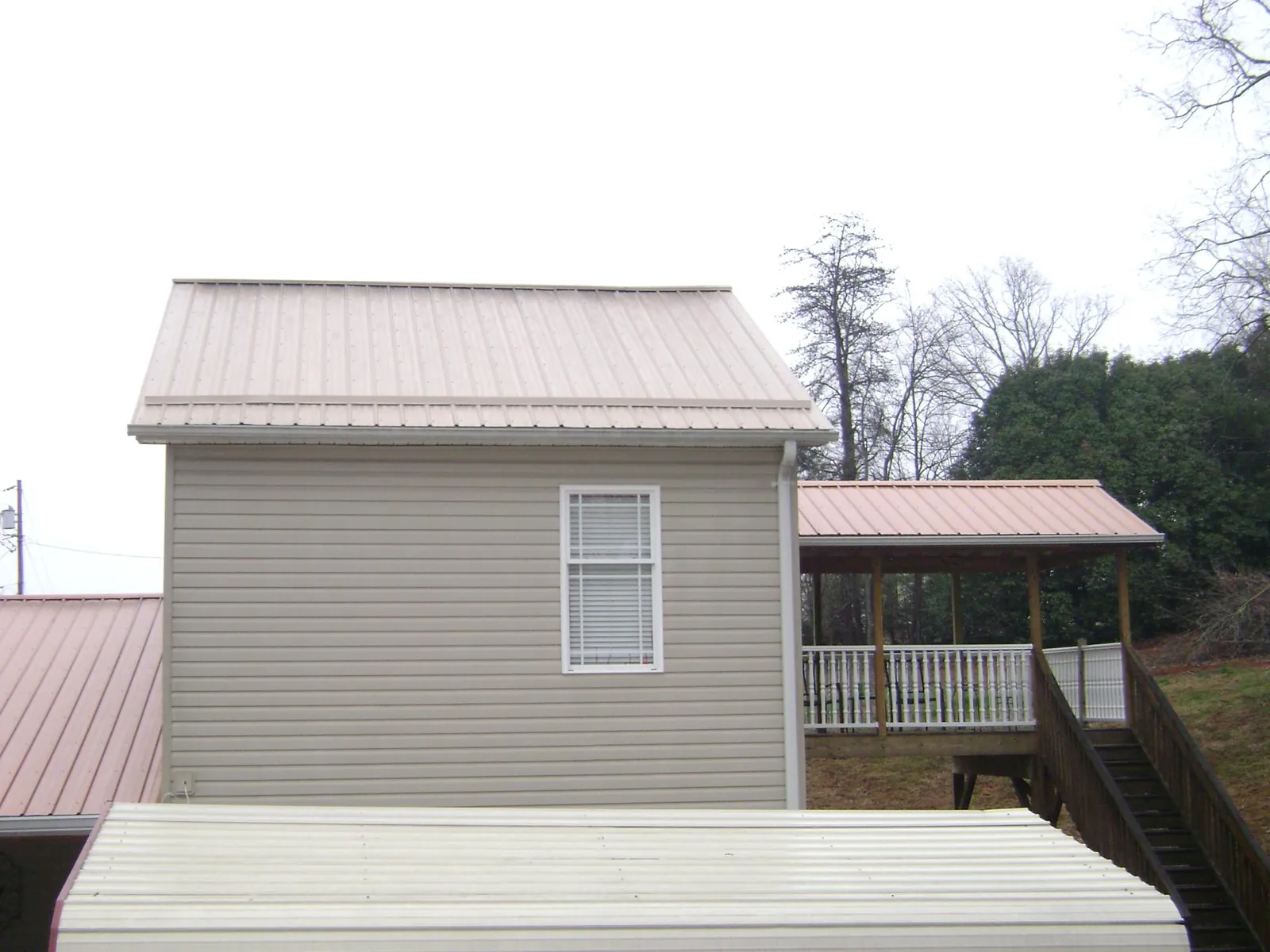 Tan metal roofs on a two story addition and attached porch, from a Roof Replacement job in Big Bend